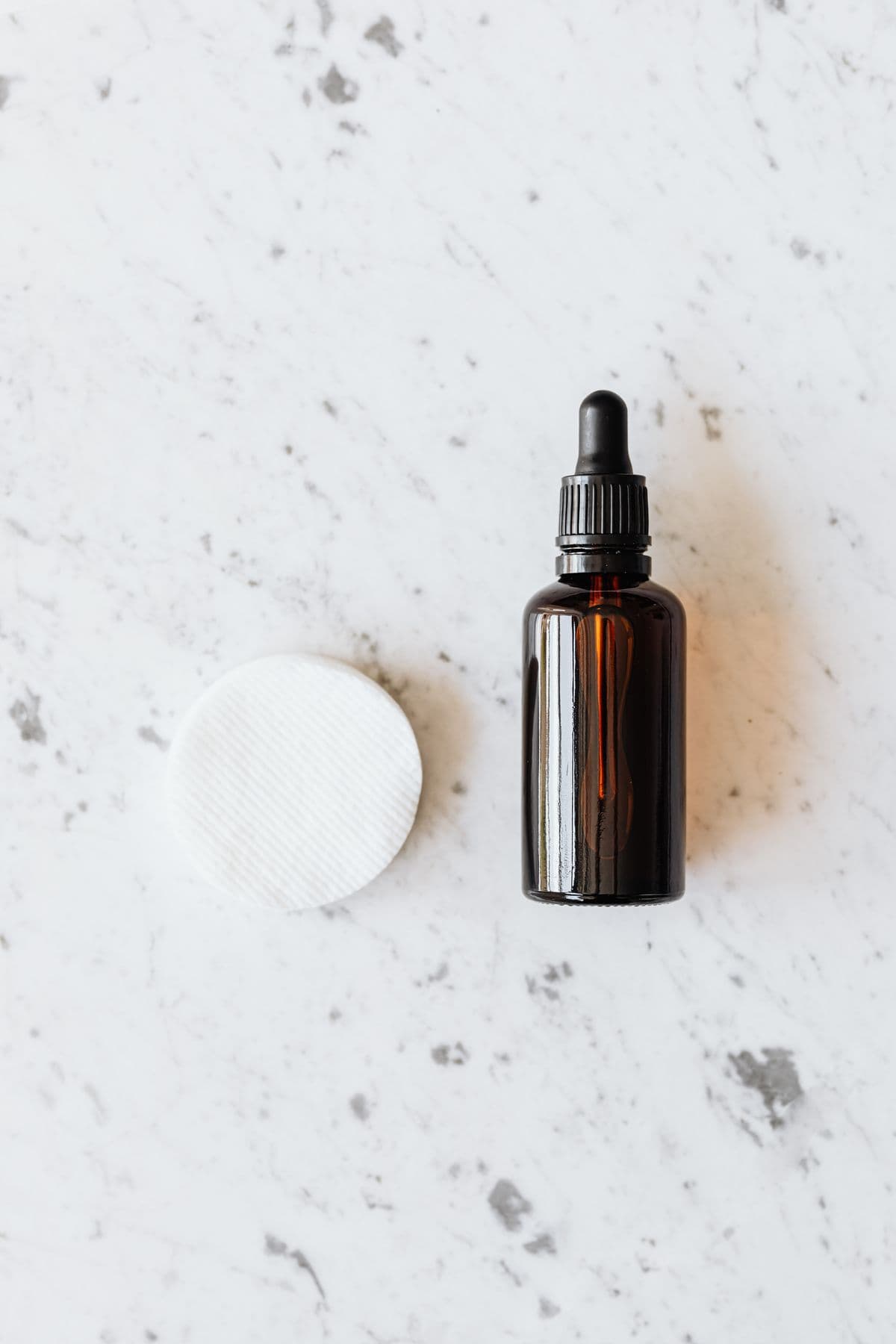 A facial serum bottle and cotton pad on a marble surface